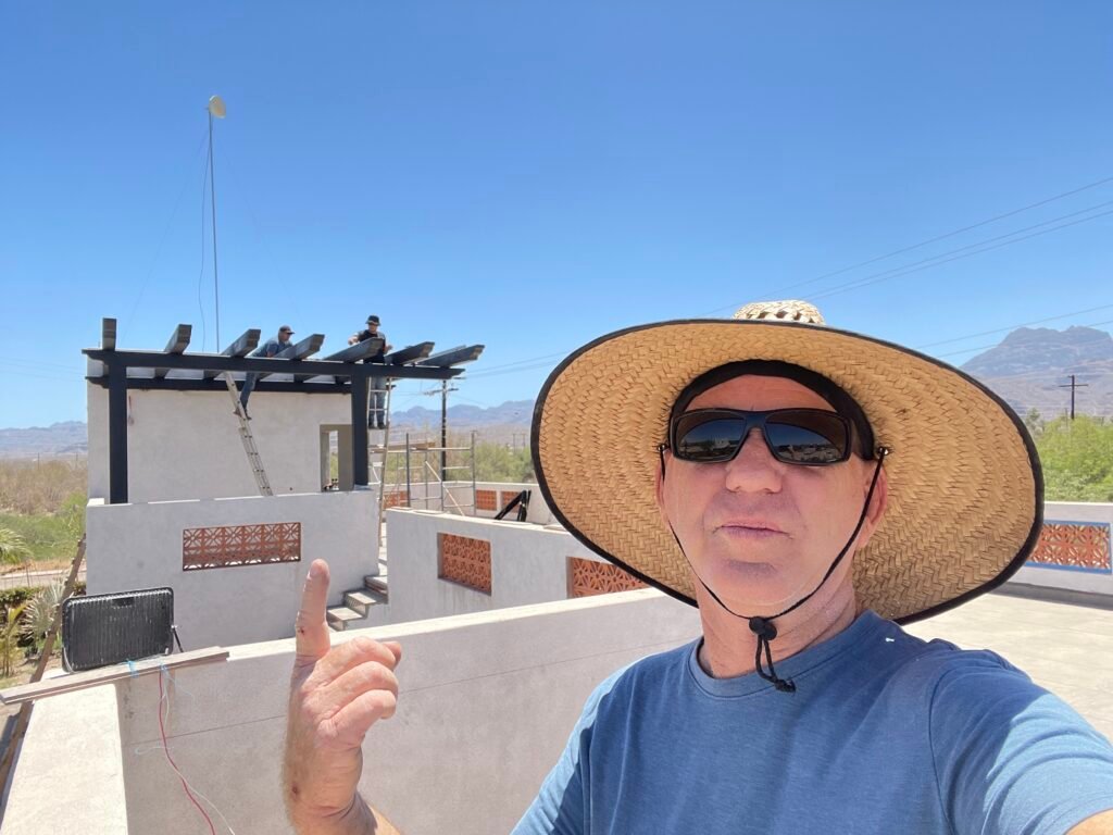 Benjamin Pride pointing at rooftop solar panels above the ocean in Cerritos, Baja California Sur, Mexico